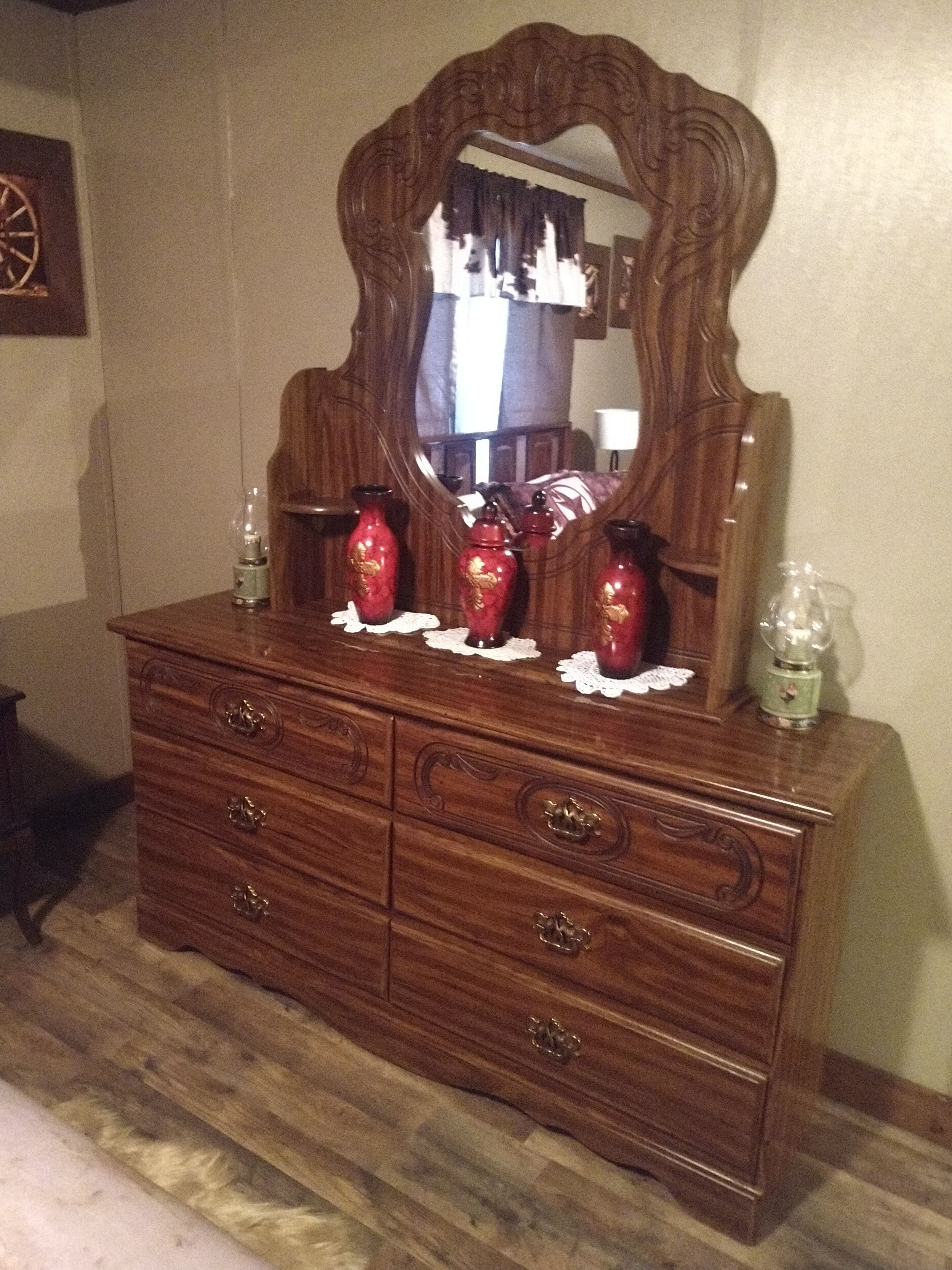 Eine Holzkommode mit einem Spiegel, drei rote Vasen und zwei Glasflaschen.