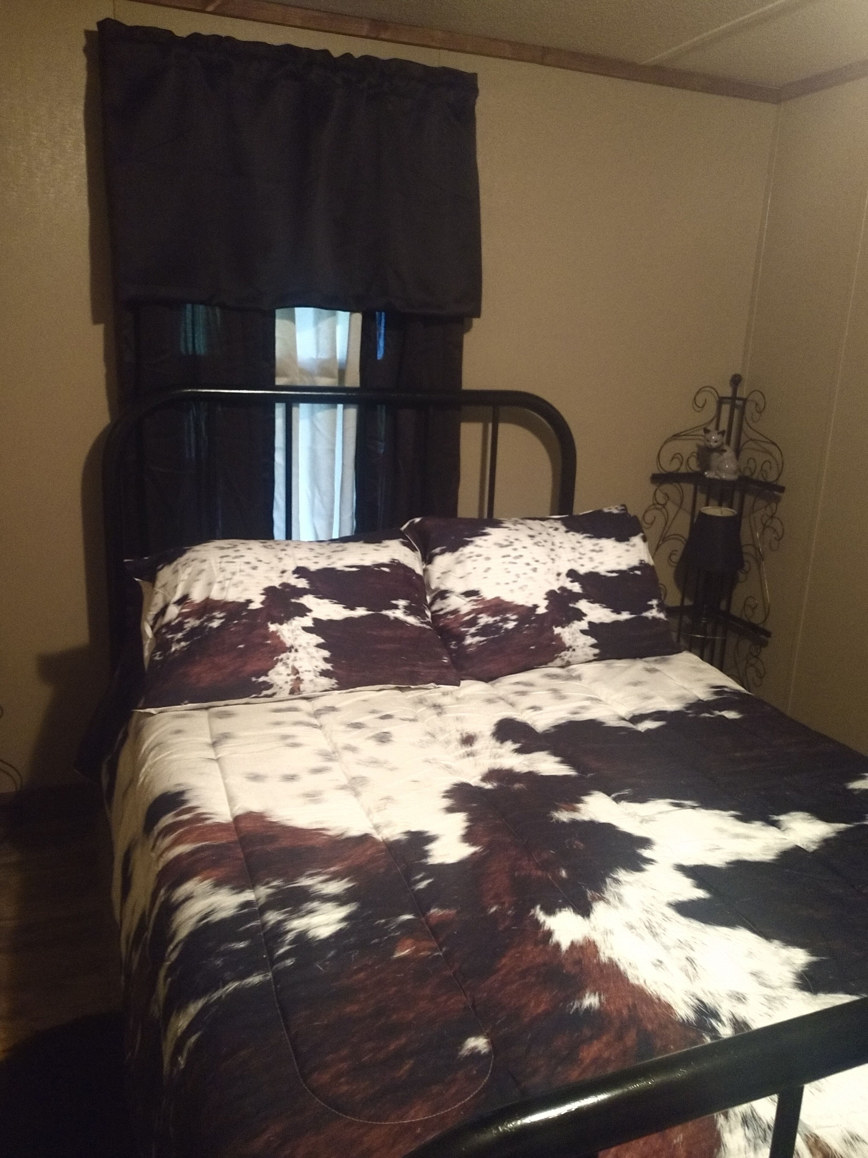 Un lit avec une couvre-lit à motifs, une tête de lit en métal et une fenêtre avec des rideaux.