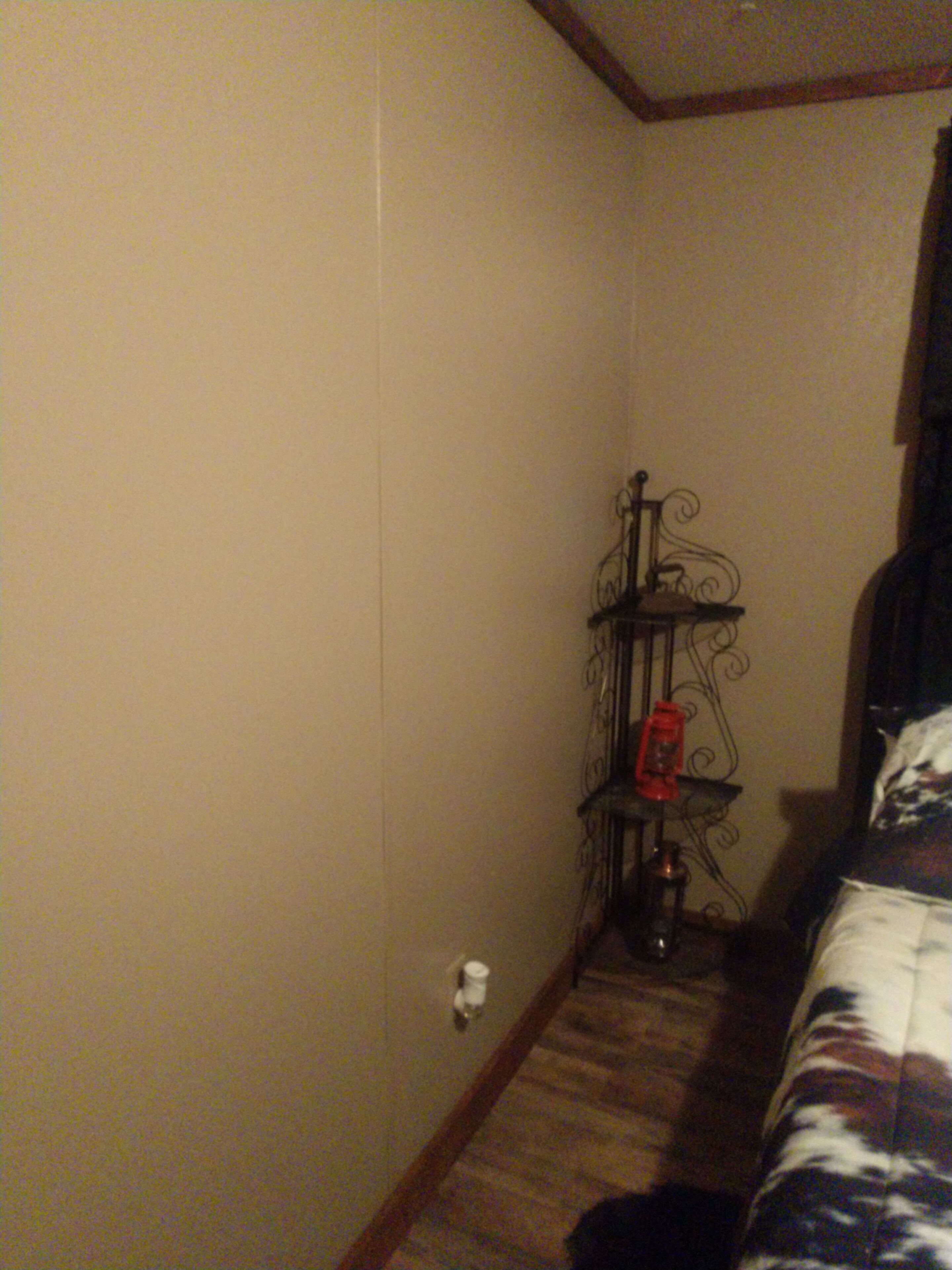 A narrow hallway with a wooden floor, a metal stand with a red object on it, and a bed with a patterned blanket.