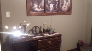 A room with a wooden dresser, a framed artwork of a cowboy hat, a steering wheel, and a guitar. - Cozy , comfortable, and warm with unique features and plenty of amenities! (Mountain City)