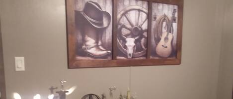 Una habitación con un aparador de madera, una obra de arte enmarcada de un sombrero de vaquero, un volante y una guitarra.