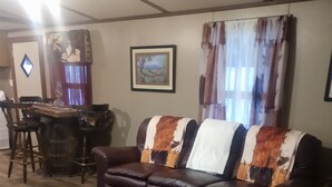 A living room with a brown leather sofa, a dining table with chairs, a framed picture on the wall, and a window with curtains. - Cozy , comfortable, and warm with unique features and plenty of amenities! (Mountain City)