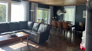 Olohuoneessa on tumma nahkasohva, puinen sohvapöytä sekä ruokailutila, jossa on puinen pöytä ja tuolit.