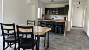 A modern kitchen with dark cabinets, a wooden island, and a dining area with black chairs and a wooden table.