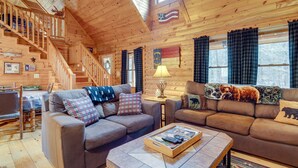 L’intérieur d’un chalet accueillant, avec un escalier en bois, deux canapés, une table basse et un coin repas.