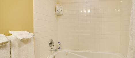 Un baño con bañera, azulejos blancos, un cabezal de ducha y dos botellas de Dove para el cuerpo en un estante.