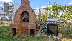 Un espace de cuisson extérieur en briques, doté d’un barbecue et d’un mur en pierre.