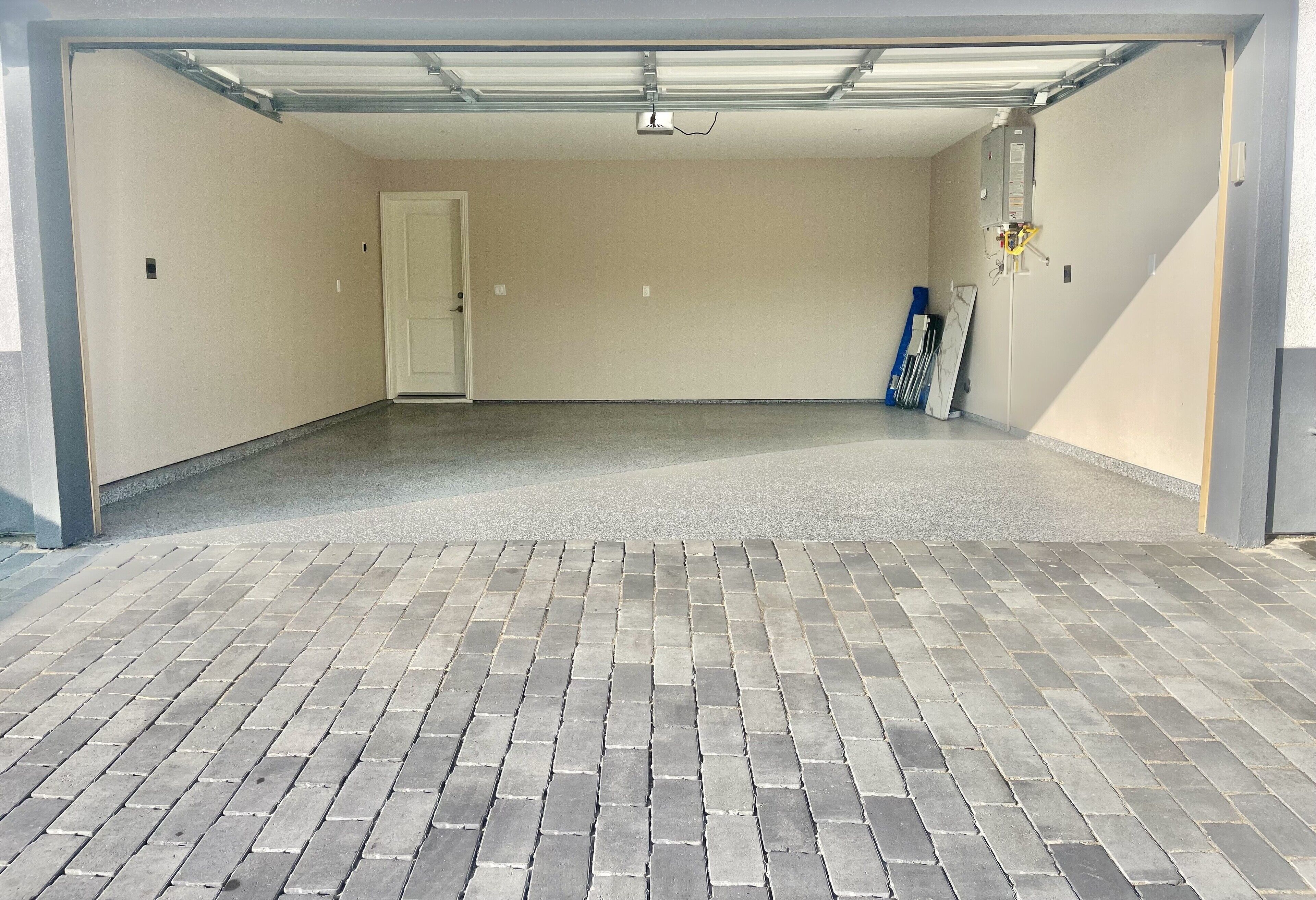 A garage with a tiled floor, a white door, and a ceiling with fluorescent lighting.