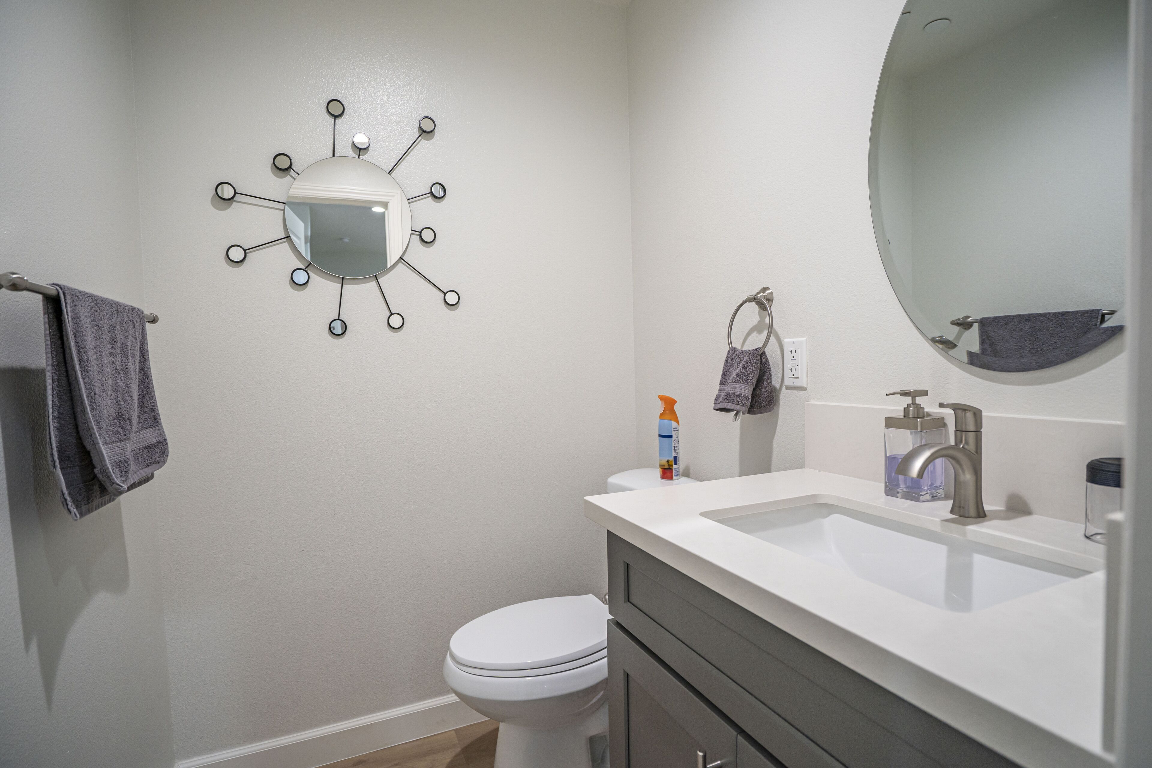 Un baño con un inodoro blanco, un lavabo blanco con un espejo arriba y una lámpara de pared.