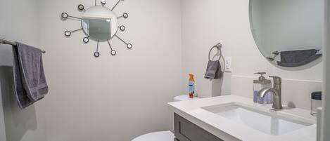 Un baño con un inodoro blanco, un lavabo blanco con un espejo arriba y una lámpara de pared.
