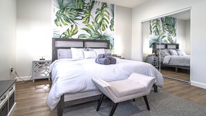 A modern bedroom with a large bed, a nightstand, a mirror, and a tropical leaf wallpaper. - Disney Luxury 3 Bedroom - Comfortable 12 Guests + EV (Midway City)