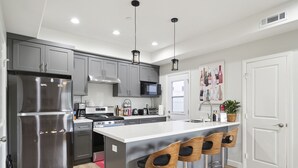 A modern kitchen with grey cabinets, stainless steel appliances, and a central island with bar stools. - Disney Luxury 3 Bedroom - Comfortable 12 Guests + EV (Midway City)