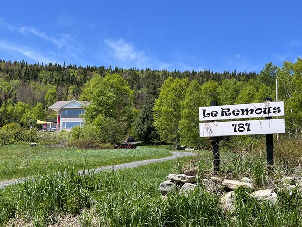 A sign reading "Le Remous 181" in a natural setting with a house in the background.
