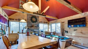 A cozy cabin interior with a wooden dining table, leather chairs, a stone fireplace, and a large window. - Duplex Unit, 2 Mi to Chittenden Reservoir! (Chittenden)