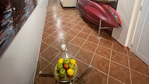 A hallway with tiled flooring, a wall-mounted painting, kayaks, a glass table with fruit, and an exit sign. - Shorebreak Hotel (Aguadilla)