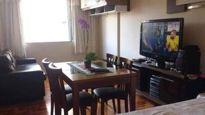 Une chambre d’hôtel comprenant un lit, une télévision, une table à manger avec des chaises, un canapé et une plante en pot.