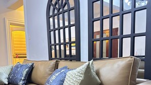 Un sofá de cuero color bronce con cojines estampados, situado frente a una ventana con diseño de celosía negra.