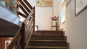 Eine Holztreppe mit Handlauf, die zu einer Zwischenebene mit einem gerahmten Gemälde und einem Stuhl führt.