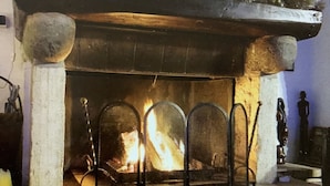 Ein Steinkamin mit Feuer, flankiert von zwei Steinpfeilern, und ein gestreiftes Sofa davor.