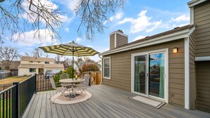 Une terrasse en bois avec une table et des chaises, un parasol et une porte-fenêtre coulissante.