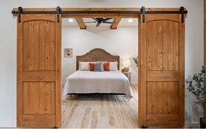 Een slaapkamer met een houten bedframe, een plafondventilator en een nachtkastje met een lamp.