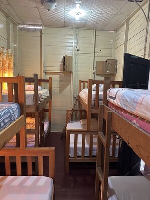A cabin interior with bunk beds, a wooden door, and a ceiling light fixture. - Hostel Caribbean Beach (Bocas del Toro)