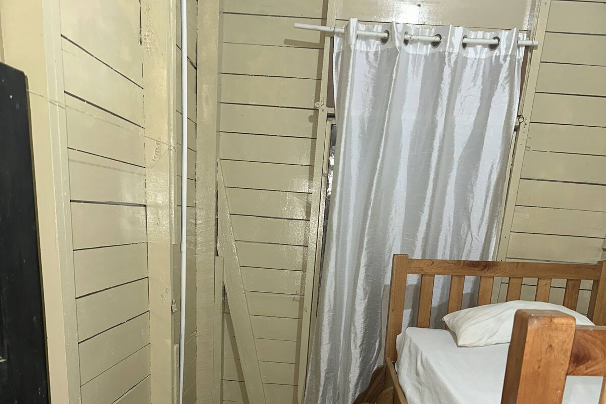 A small, single-occupancy room with a wooden bunk bed, a white curtain, and a door with a black frame.