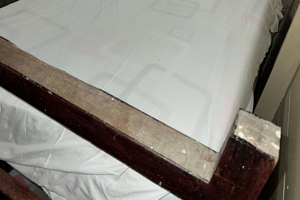 A single bed with a wooden frame and white bedding in a room with plain walls and a curtain.