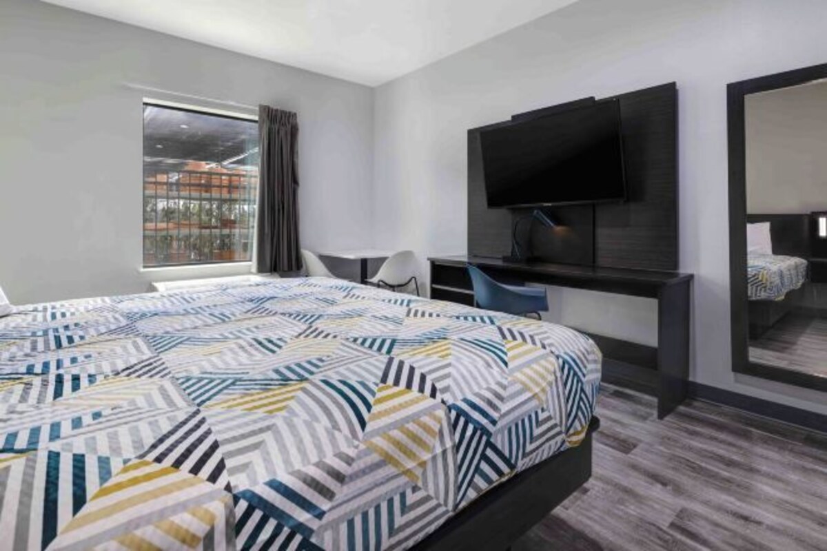 A hotel room with a large bed, a desk, a chair, a TV, and a window.