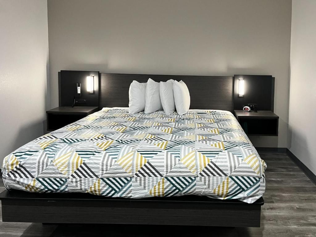 A modern bedroom with a geometric patterned bedspread, two bedside tables with wall-mounted lamps, and a dark headboard.