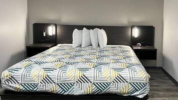 A modern bedroom with a geometric patterned bedspread, two bedside tables with wall-mounted lamps, and a dark headboard.