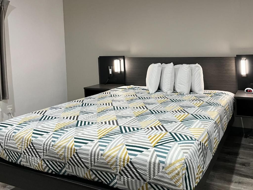 A neatly made bed with a geometric patterned bedspread, two bedside tables with lamps, and a dark headboard.