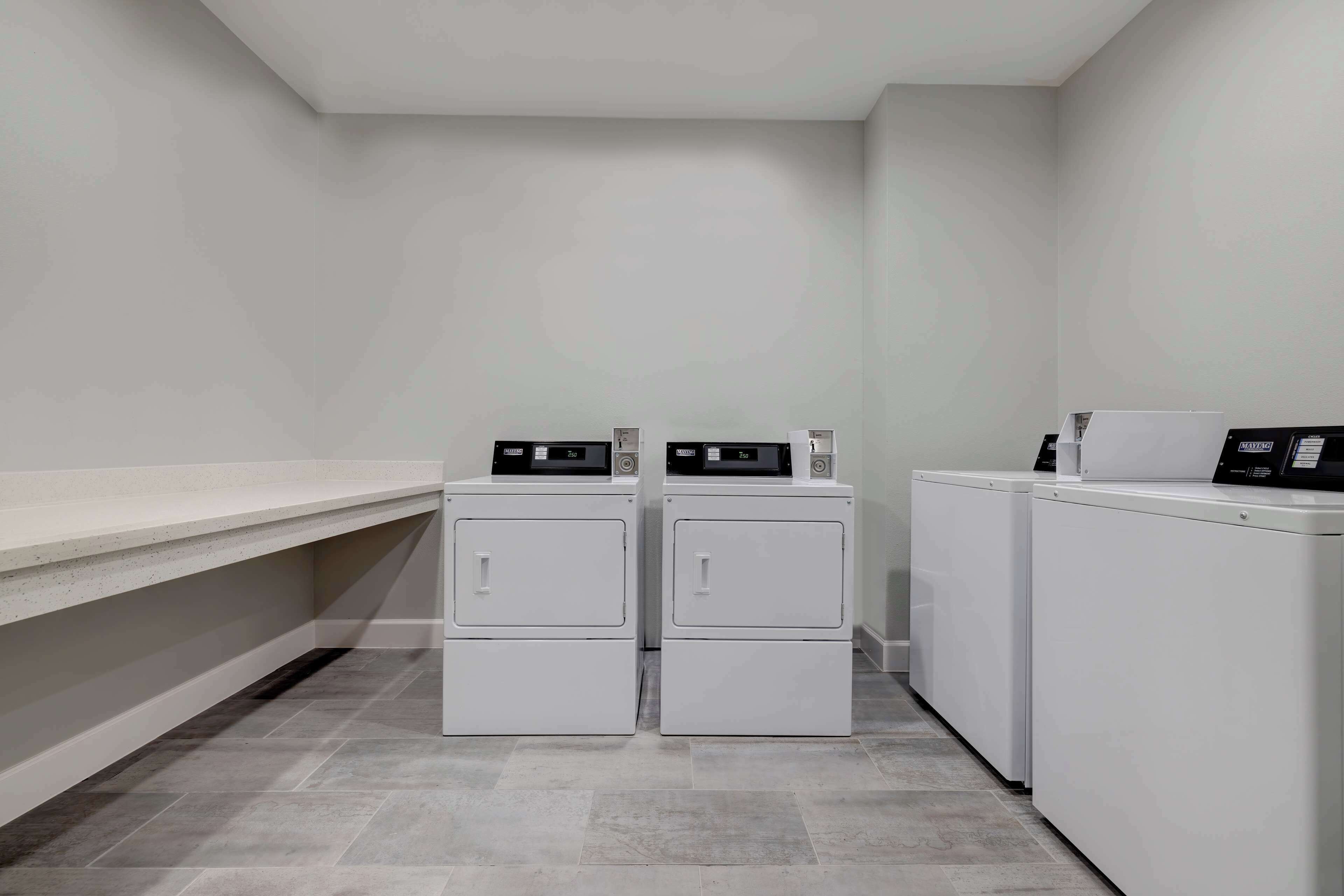 A laundry room with two stacked washers and dryers, a white bench, and a tiled floor.