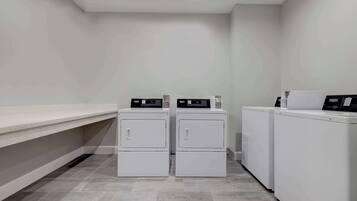 A laundry room with two stacked washers and dryers, a white bench, and a tiled floor.