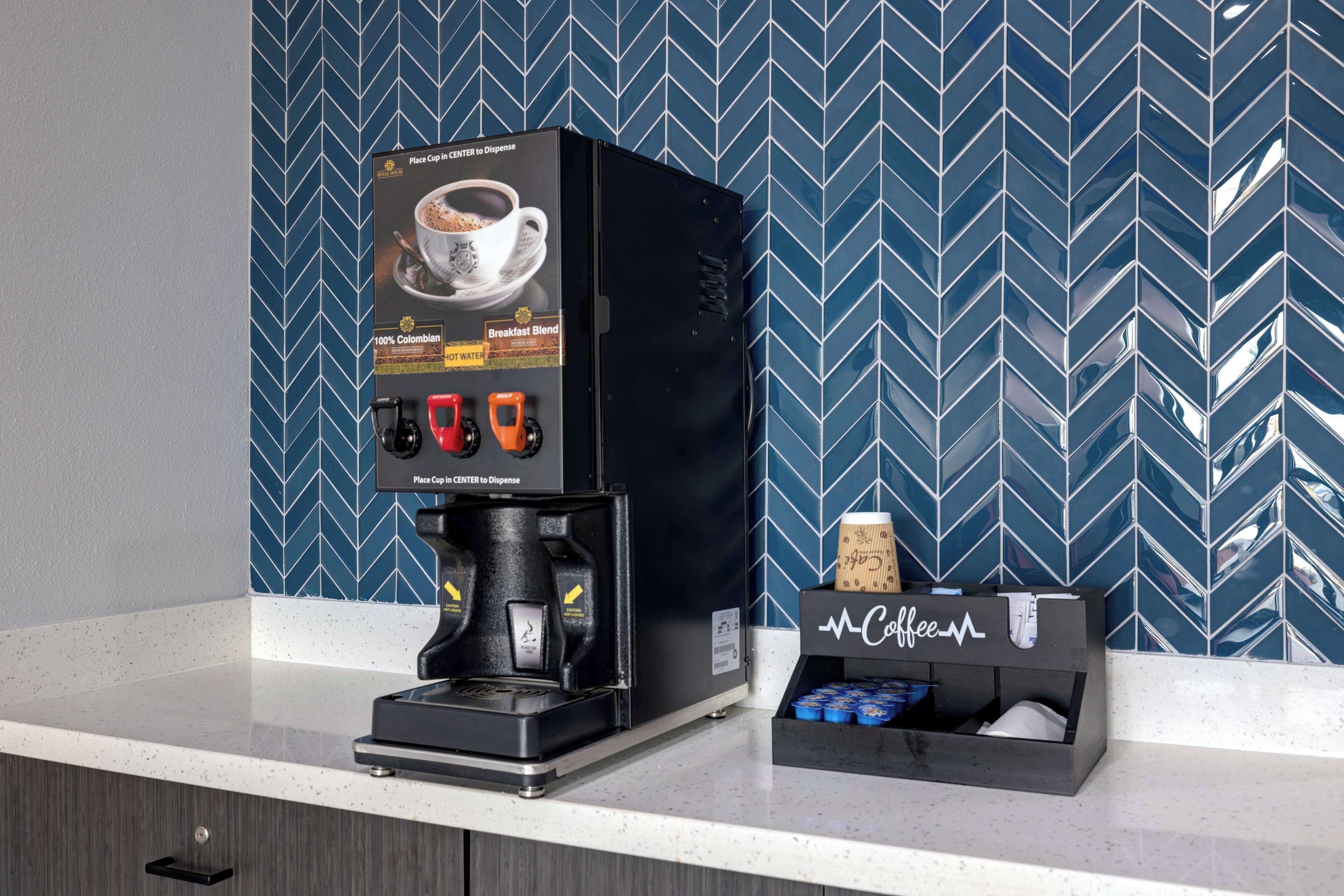 Een koffieapparaat met een display voor koffiekopjes en een doos met het merk McCoffee op een aanrecht.