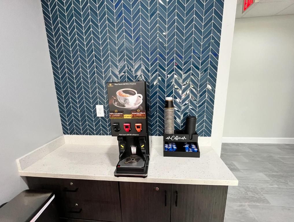 A coffee machine and a coffee dispenser on a countertop with a patterned wall in the background.