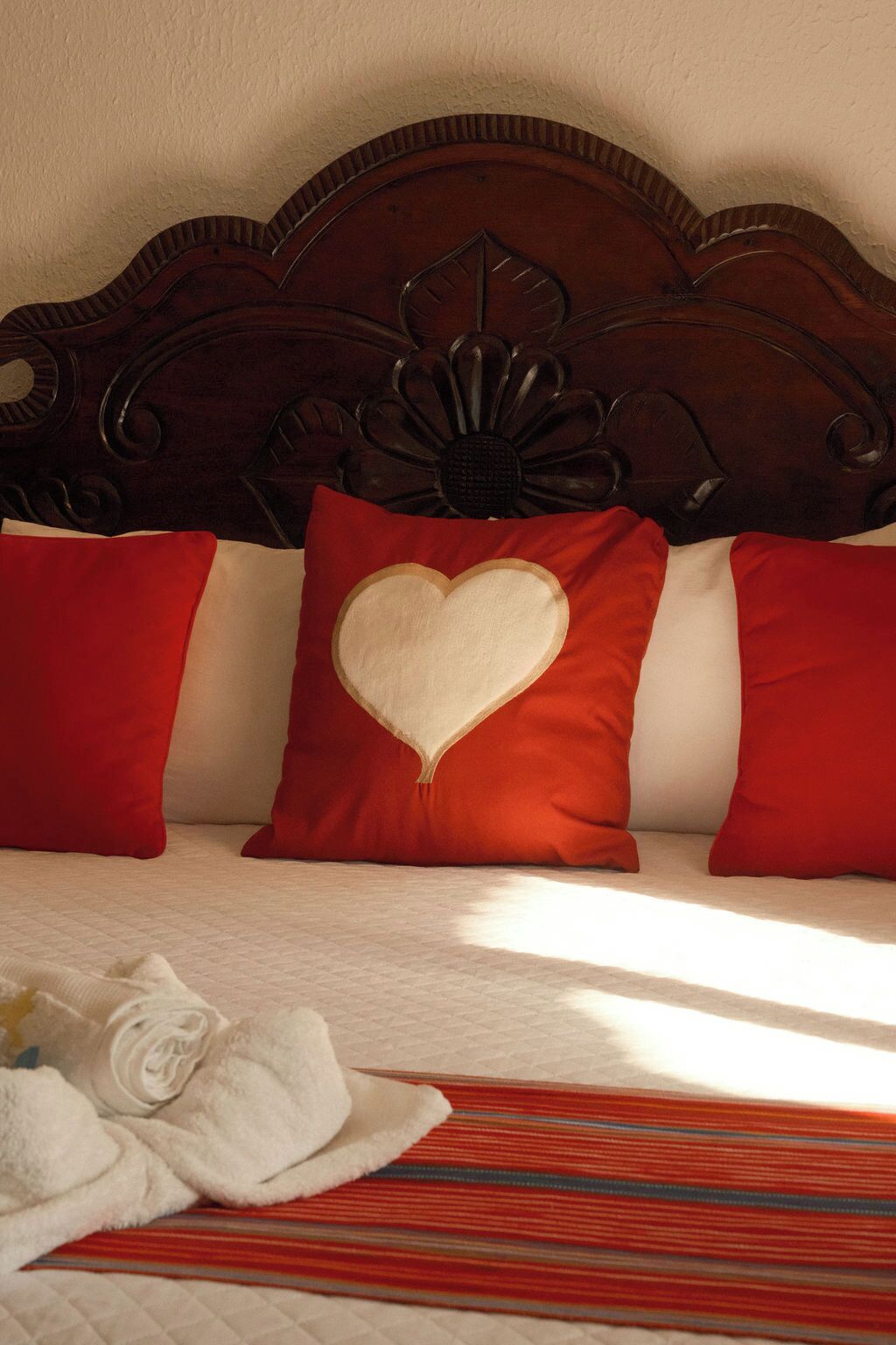 A bed with red and white pillows, a wooden headboard, and a striped rug.