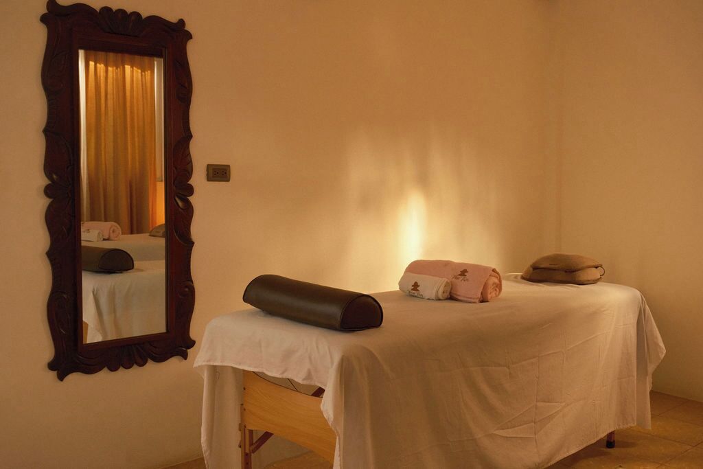 Una habitación con cama, una camilla de masaje, un espejo grande y una ventana con cortinas.