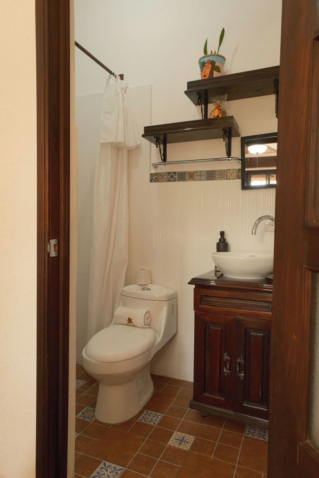 A bathroom with a toilet, a sink, a shower curtain, and a shelf with a potted plant.