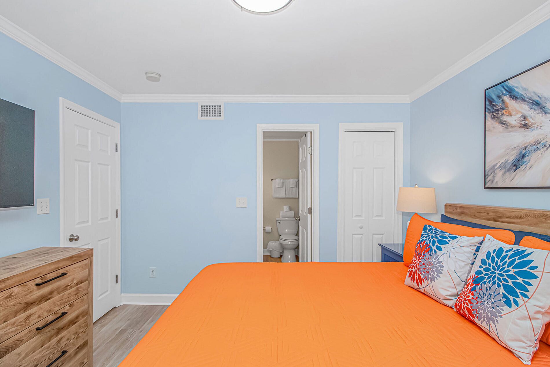 A bedroom with a bed, a wooden dresser, a door, and a bathroom visible through an open door.