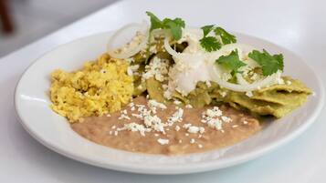 Un plato de comida con huevos revueltos, frijoles refritos, aguacate, crema agria, cebolla y cilantro.