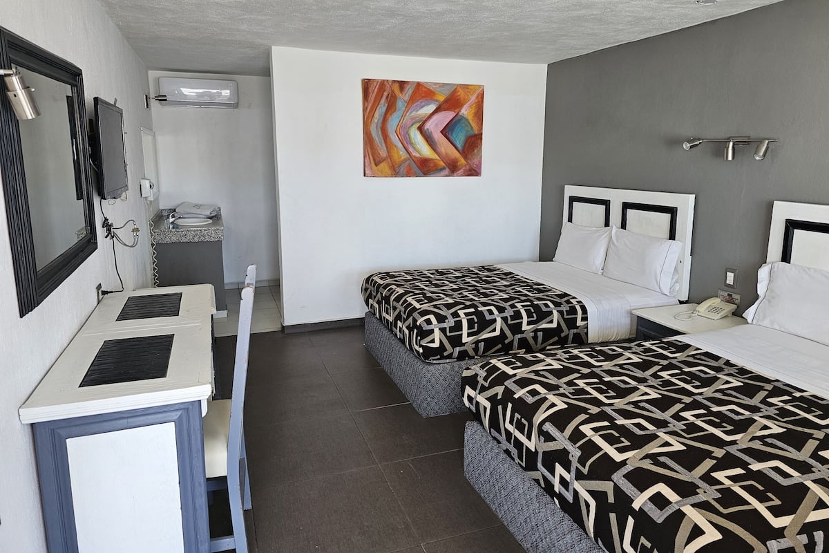 A hotel room with two beds, a desk, a chair, a telephone, and a painting on the wall.