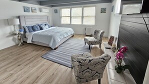 A modern bedroom with a large bed, a sitting area with a chair, and a small table. - Charming, luxe, modern home near Naval base, Six flags, Casino, Gurnee Mills (Waukegan)