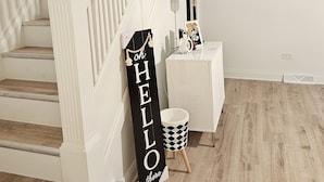A staircase with white railings and wooden steps, a black and white sign that reads "HELLO there", a small white side table with a lamp, and a black and white patterned trash bin. - Charming, luxe, modern home near Naval base, Six flags, Casino, Gurnee Mills (Waukegan)