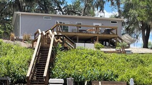 Ein Ufergrundstück mit einer Holzterrasse, einer Treppe zu einem überdachten Bereich und einem Steg, der ins Wasser führt.