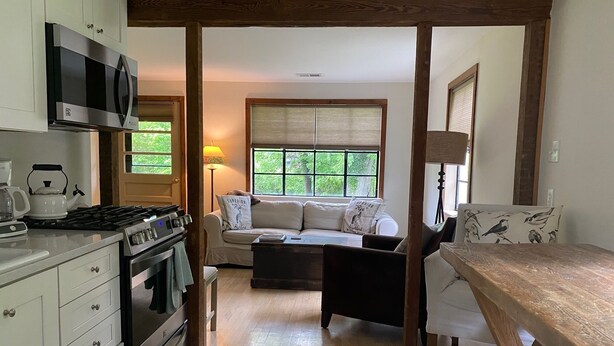Cocina compacta con microondas, hervidor y estufa, que da paso a una zona de estar con sofá y mesa.