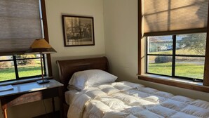 Una cama individual con cabecera de madera, un escritorio con lámpara y un cuadro en la pared.