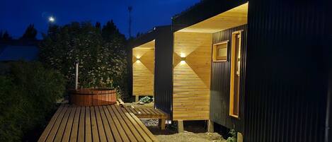 A wooden deck leading to a building with two rooms, one with a window and a door, and a small outdoor seating area with a table and chairs.