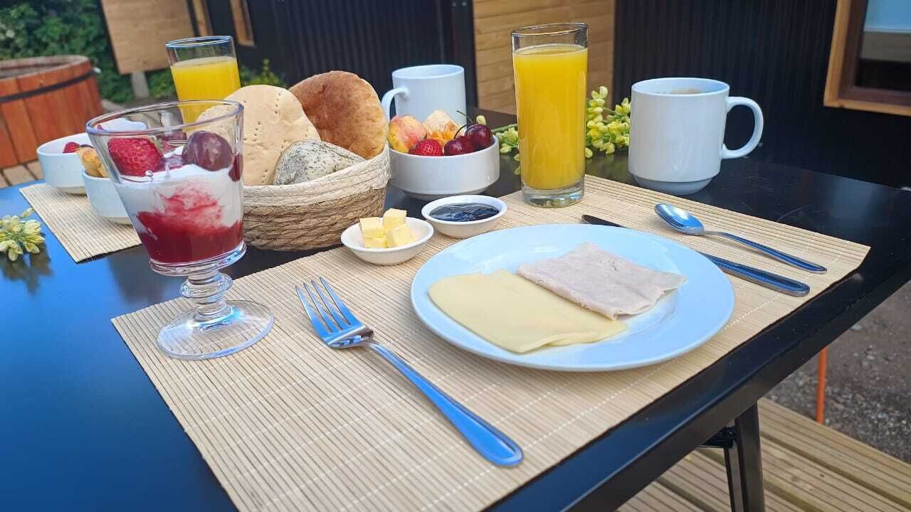 Una mesa de desayuno con un plato de jamón y queso, un vaso de jugo de naranja, un tazón de fruta y un vaso de jugo rojo.