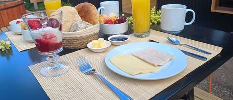 A breakfast table with a plate of ham and cheese, a glass of orange juice, a bowl of fruit, and a glass of red juice.